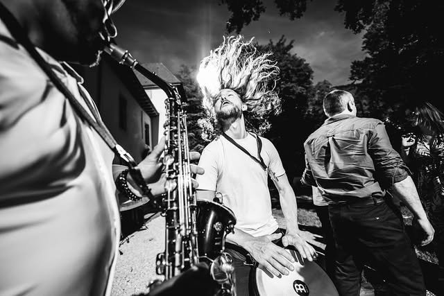 Un saxophoniste et un percussionniste jouent en extérieur lors d'un mariage, photographie en noir et blanc.